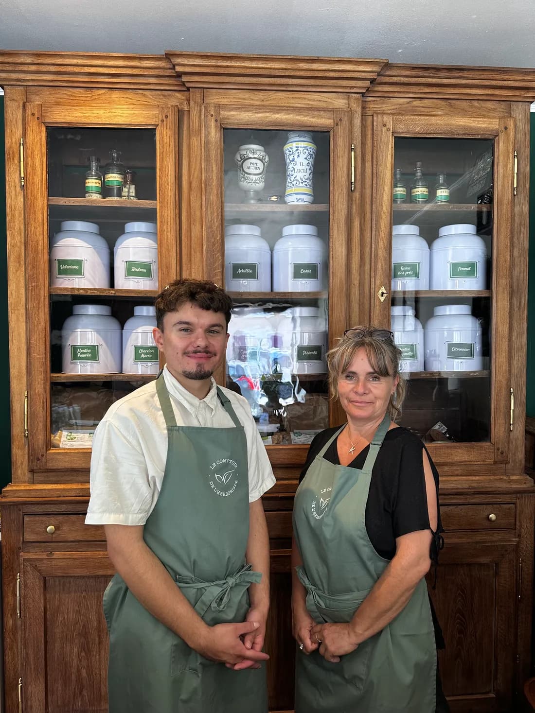 Virginie et Mathieu du Comptoir de l'Herboriste, devant l'armoire d'apothicaire garnie de plantes